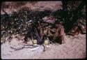 Two women sitting next to a fire, cooking, with tsama melons on the ground next to them, used as double-boilers (copy of slide 11E-241)