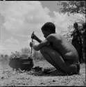 Man squatting, cooking, stirring the food in an iron pot with a stick