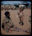 Expedition: Boy eating a lollipop, standing next to a woman who is sitting, with a group of people sitting next to an expedition truck in the background