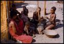 Women and boys pounding meal in log