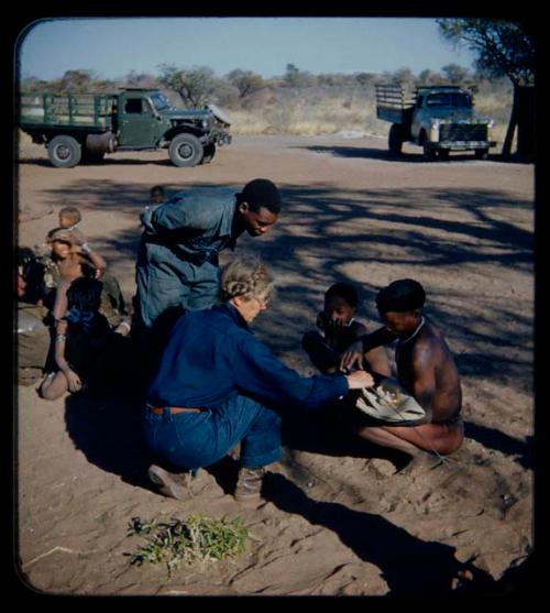 Expedition: Man receiving a gift of wire from Lorna Marshall, with a child and Kernel Ledimo watching