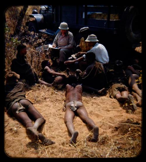 Expedition: J. O. Brew interviewing a man near a truck, assisted by two interpreters, with a group of people watching them