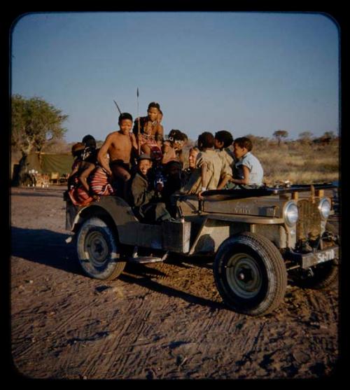 Expedition: Group of people wearing clothes gifted by the Marshall family, John Marshall, Ngani, and //Ao riding in Jeep