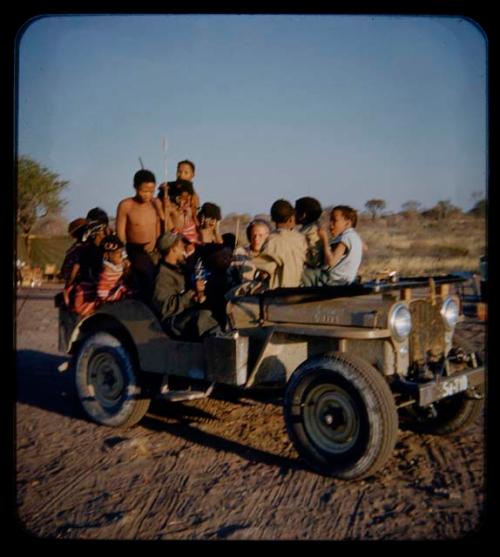 Expedition: Group of people wearing clothes gifted by the Marshall family, John Marshall, Ngani, and //Ao riding in Jeep