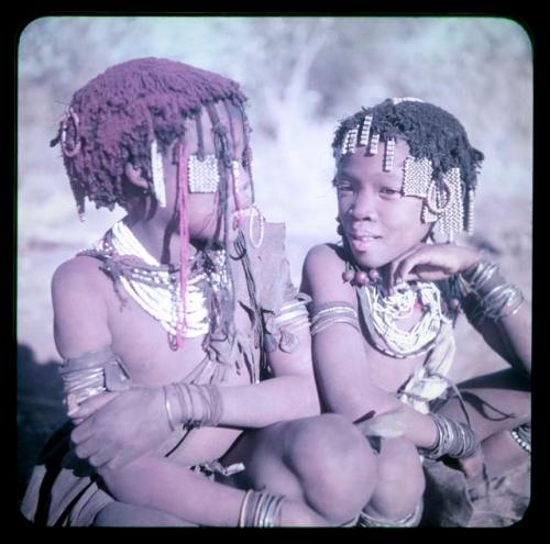 Children, Portraits: ≠Gisa sitting with a girl wearing white necklaces and bead ornaments hanging down across her face, with red powder in her hair