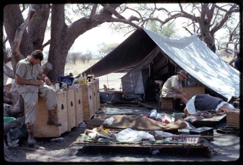 Wulf Haacke and C. J. Mathias sitting in the expedition camp in front of a tent