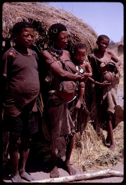 Group standing before ǂToma's hut, including ǂToma and !U, close-up view