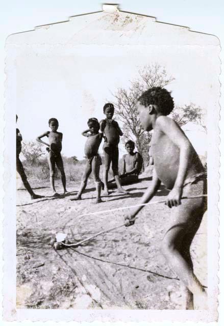 Boy pushing a toy car, with a group of boys watching him