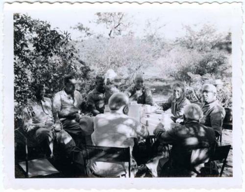 Group of people sitting around a table in the expedition camp, including L. F. Maingard, Frank Ramsden, Lorna Marshall, Thomas Hardbattle, Theunis Berger, H. Ramsden and Bill D.