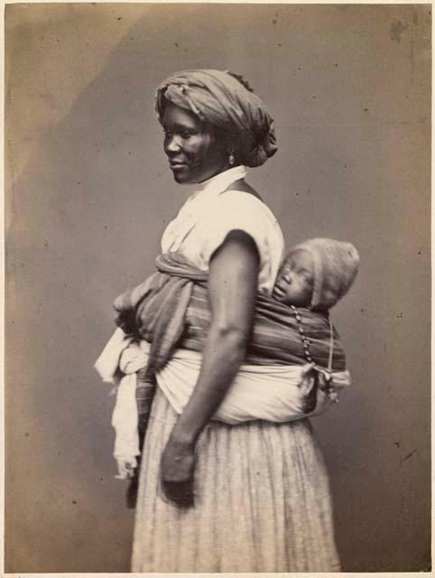 Woman standing, with a baby tied to her back, profile