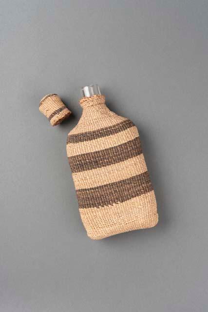 Bottle (A) completely covered in basketry twining with basketry lid (B)