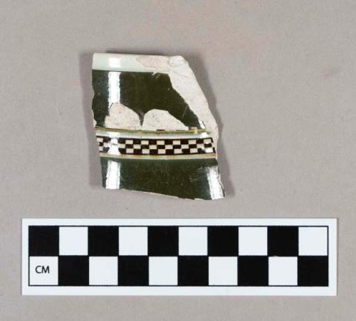 Ceramic, pearlware rim sherd with part of spout, exterior is factory decorated slipware with dark green field and black and white checkered banding