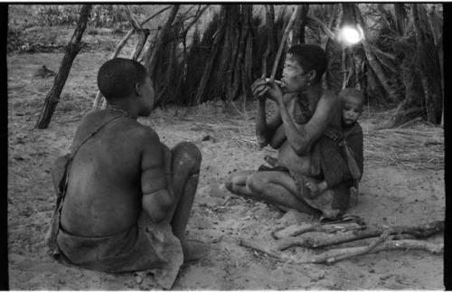 Rukan and Genitsu seated; Genitsu lighting a pipe