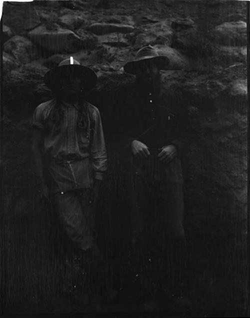 Two men standing in front of a rock wall