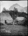 Woman holding a child, standing in front of a house in Namosi