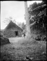 Woman carrying a child on her back, with houses in the background