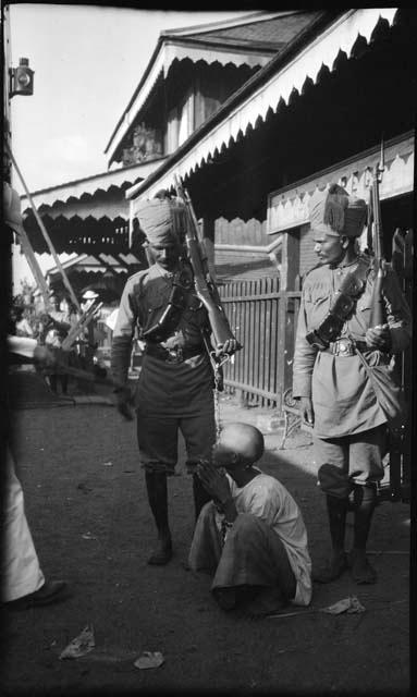 Two guards with a prisoner in front of a building