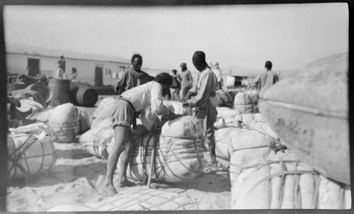 Men working with large bundles on shore, with an Irrawaddy Flotilla Company boat in the background