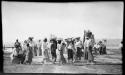 Group of people carrying baskets and bundles on their heads, with a steamboat in the background