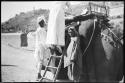 Woman climbing a ladder onto an elephant, with two people standing next to her