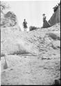 Man and woman wearing Western clothing, standing on a rocky hill, with people at the top of a rock wall watching them