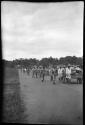 People pulling carts down a road, with men in uniforms walking next to them