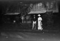 Man and woman dressed in Western clothing, standing in front of a building