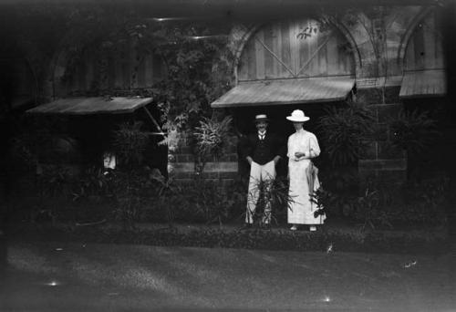 Man and woman dressed in Western clothing, standing in front of a building