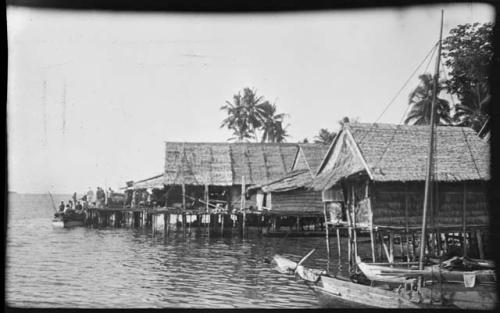 People on a boat next to buildings on stilts