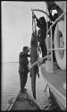 Men standing next to a crocodile hanging from the rail of a ship