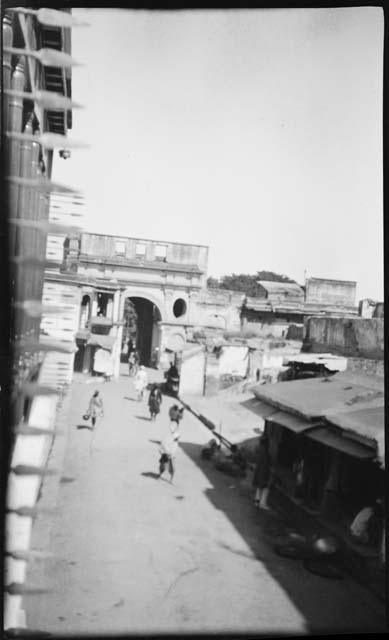 People walking down a street, with a stone arch in the background