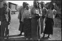 Group of people standing, with a railroad car in the background