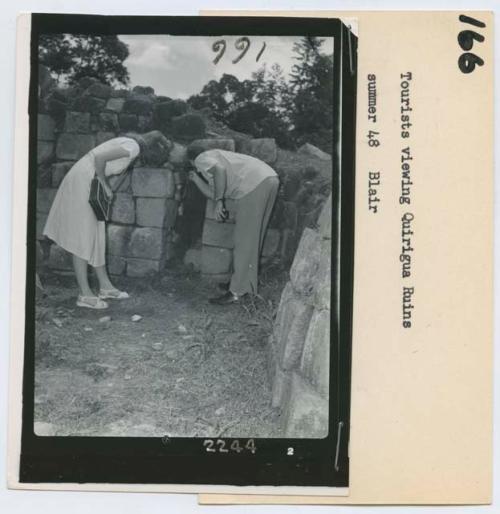 Two people leaning over to look at an opening in the stones