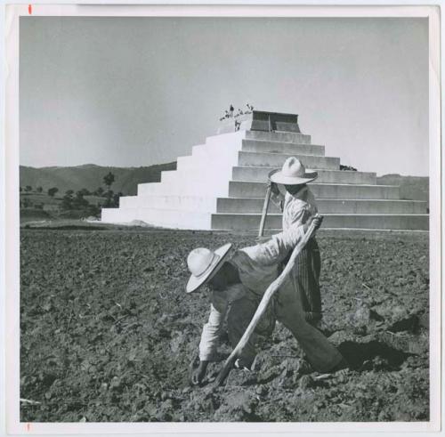 Outdoor image depicting two men working in the ground with Zaculeu in background