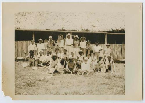 Photograph of crew, group of men standing and sitting in front of a building