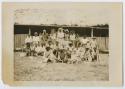 Photograph of crew, group of men standing and sitting in front of a building