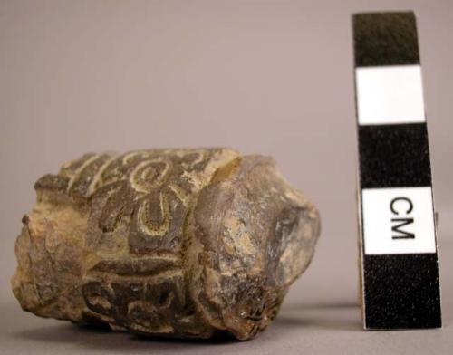 Solid clay cylinder covered with heavily incised decoration.