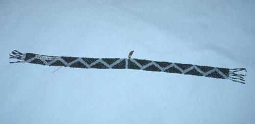 Bead armlet (?)--white zigzag pattern on dark green; beaded fringe at ends