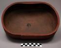 Brown wooden dish with curved sides and black linear designs inside