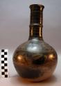 Bottle. grey clay. black slip with gold design. spherical with cylindrical neck.