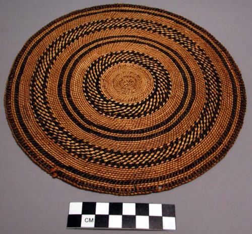 Circular basketry mat with yellow and black grasses