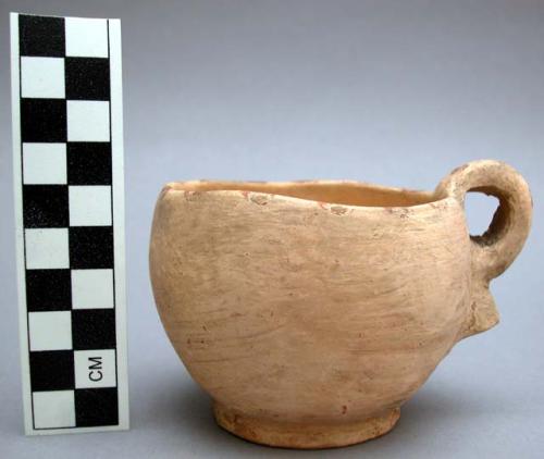 Single-handled ceramic cup. beeige slip with red dots around rim of cup.