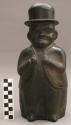 Black ceramic vessel in the form of a standing male figure wearing a hat and jac