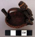 Miniature bowl with stirrup handle and human effigy perched on rim. Polychrome.