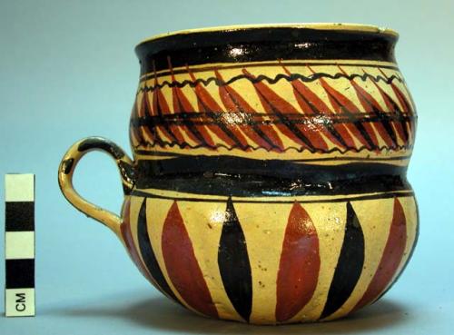 Mug. Grey clay, yellow glaze with brown and black design, with handle.