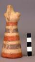 Pottery bird figure on top pottery cone. cone has red, white, blue bands.