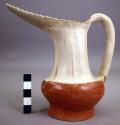 Pottery pitcher. Saw toothed edge on lip; red base, buff top.